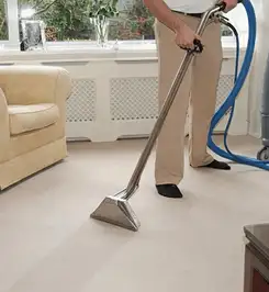 Professional carpet cleaner using a hot-water extraction wand and hose machine in a living room in Mesa, AZ.