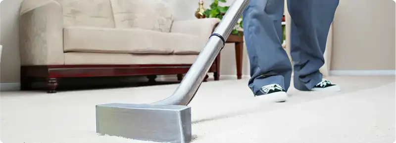 Carpet cleaning technician using a hot-water extraction wand on a light-colored carpet in a living room, Mesa, AZ.