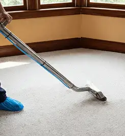 Steam carpet cleaning technician using a hot-water extraction wand on a residential carpet, wearing blue protective shoe covers Mesa, AZ.