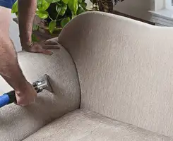 Professional upholstery cleaner deep-cleaning a fabric sofa with a handheld extraction tool and hose in Mesa, AZ.